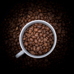 cup full of coffee beans resting over sack of coffee beans