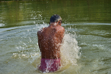 A man bathing in a natural lake, refreshing himself from heat of summer in summer season in rural India, at Nature Reserve.