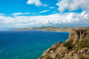Obraz premium Crimean summer sunny mountain and sea landscape under thick clouds with a town in the distance, shot on a holiday trip