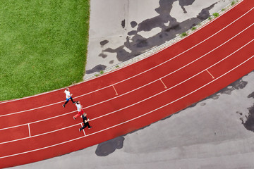 three runners training in a stadium on a red treadmill after the rain, top view