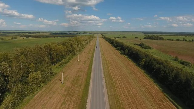 Flying over the straight forest road. The movement of cars on the road. Top view on cars, trees, field. Summer video from the drone. Rural landscape.