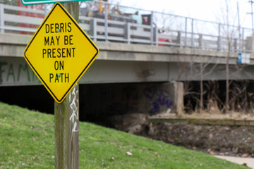 Utica, Michigan/ United States - April 17 2019: Graffiti on bridge that goes over trail with warning sign about path.