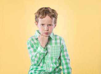 Little boy in green shirt on yellow background with unhappy expression