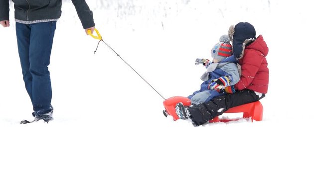 Detail of father feet on snow, parent pull sleight with children, colored joy