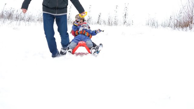 Portrait of happy children on sleight, father pull sledge, detail of parent feet
