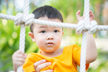 Fototapeta premium Little Asian toddler boy climbing on the rope at playground
