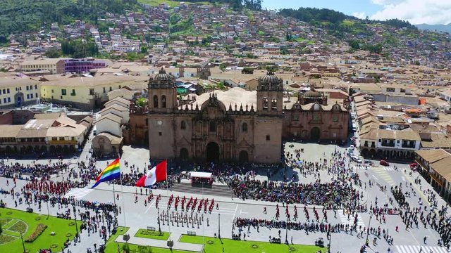 Aerial view of Cusco's main plaza with parade and crowd of people watching the national flag raising act. Marching band, Peruvian and Tahuantinsuyo flag weaving at the Sunday ceremony.