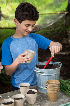 Boy scooping soil into pots to plant seeds in the garden
