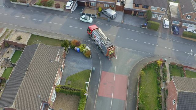 A bin lorry, refuse collection vehicle makes it way up the road as men load recycling bins into the waste compactor in a middle/working class area in the city