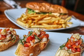 Dieses einzigartige Foto zeigt im Vordergrund die Bruschetta-Vorspeise und im Hintergrund sehen Sie ein Käsesandwich mit Pommes