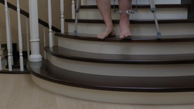Descend the stairs on crutches with a broken leg in an external Ilizarov fixative. Close-up.