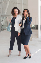 Two serious business women talking on phone and drinking coffee