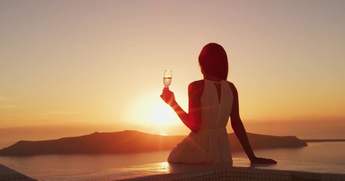 Luxury lifestyle - Woman drinking champagne at sunset. Elegant lady holding wine class looking at sunset over the ocean enjoying amazing view on luxury travel vacation. SLOW MOTION shot on RED EPIC.