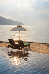 Beach beds with sun flare twilight time. Beds are on sand between ocean and swimming pool.