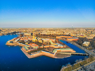 Fototapeta premium Beautifull aerial view of the Petropavlovsky fortress in sunny spring day. Golden tall spire of famous Peter and Paul Cathedral on the blue sky background. Historical centre of St. Petersburg, Russia.