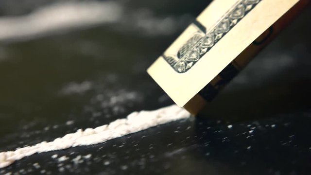 Addict sniffs  line of cocaine through a rolled dollar bill from a black table in room, close-up, macro. Drug abuse. Drug use, addiction, social issues. Illegal substances and dirty money. 4K