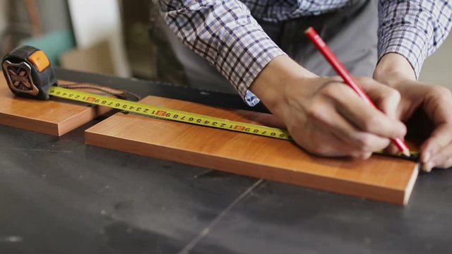 Male hands using a yellow tape measure to measure a piece of wood