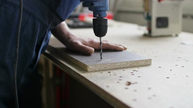 Man hands make holes in wooden board with electric drill