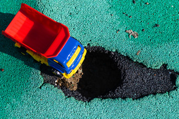Toy plastic truck with a red body stopped in front of the pit. The car can not go. Hole on asphalt. The road needs repairs