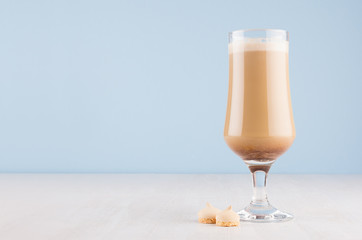 Refreshment coffee drink with cream, foam and cookies in wineglass in light blue interior on white wooden table, copy space.