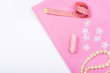 Obraz na płótnie Canvas Tailoring. Sewing accessories and accessories for sewing and needlework. Imitation jewelry, centimeter, pattern, reel with thread and fabric of pink color on a white background. Isolate, Flat Lay, Cop