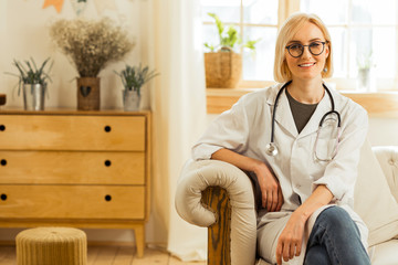 Smiling physician in a white coat sitting on the sofa