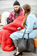 Homeless beggar with young woman listening to his sad story while sitting together on the bench...