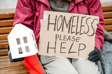 Homeless beggar holding paper house and message for help on a cardboard begging and grieving for a...