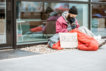 Homeless beggar wrapped with sleeping bag begging money near the business center. Concept of...