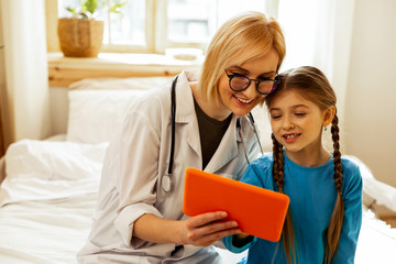 Cheerful physician looking at orange tablet along with a girl.