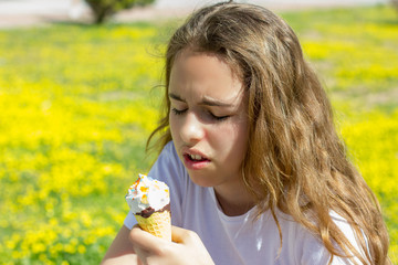 Dissatisfied unhappy teen girl eats tasteless ice cream in a waffle cone in summer. Selective focus