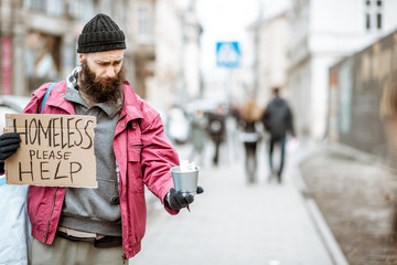 Portrait of a depressed homeless beggar with cardboard begging some money on the street in the city