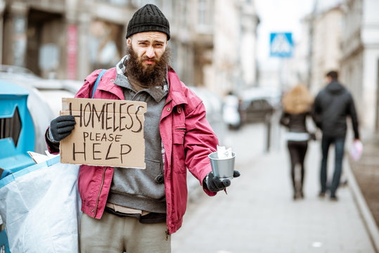 Portrait of a depressed homeless beggar with cardboard begging some money on the street in the city