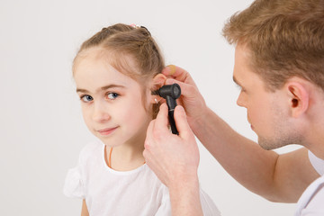 The young sympathetic otolaryngologist examines the ears of a girl - a girl of school age. People isolated on a white background