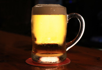 A beer glass on the wood of a bar lit from behind with drops on the glass