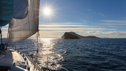 View over the bow of a sailing yacht to Isla Grosa, La Manga and the Mar Menor with the sun as backlight