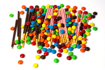 Colorful chocolate M&Ms and Pocky candy in and out of focus on white background