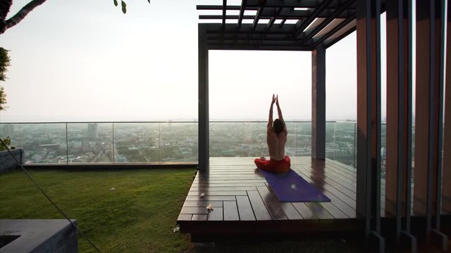 Young Caucasian man doing yoga in the morning at the gazebo on the 41st floor.
