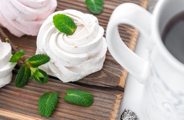 White creamy marshmallow handmade. Adorned with mint leaves. Tea in a white cup with a blue ornament. On a wooden background. Close-up.