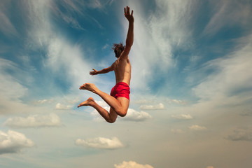 Man jumping over cloudly sky background. Outdoor adventure lifestyle. Summer fun lifestyle.