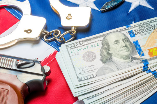 Conceptual photo of the crime and money: dollars, handcuffs and a gun on the American flag
