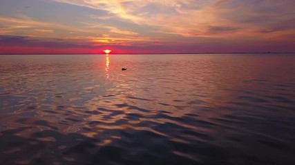 Aerial,drone shot, of a message in a glass bottle, floating in the reflecting sea. Calm, tranquil ocean and colorful dusk, in the background, in Sweden