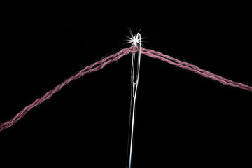 Needle with a large needle eye with wool thread on a black background. Close-up