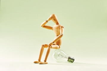 Having no idea. Wood figure mannequin sitting on an incandescent light bulb