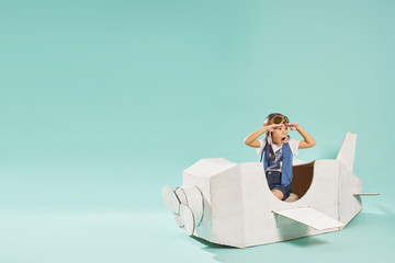Little cute girl playing with a cardboard airplane. White retro style cardboard airplane on mint...