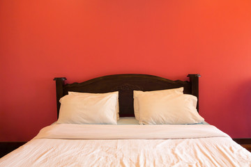 Dark wooden bed on the red wall background, white linens. Front view, copy space