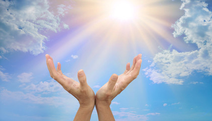 Bring sunshine into the lives of others by giving - Female cupped  hands reaching up to sunburst on a  blue sky background with plenty of copy space