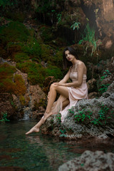 Beautiful girl posing in river. Fairytale story. Natural pool surrounded by green tree's leafs.