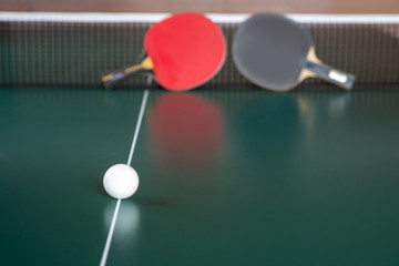 Two ping-pong rackets and a ball on a green table. ping-pong net.