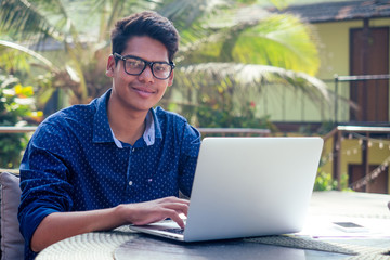 handsome and young successful indian man freelancing surfing remote work with a laptop on the beach...